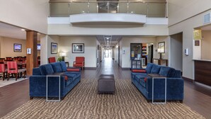 Eine geräumige Lobby mit hoher Decke, zwei blaue Sofas mit roten Kissen, einem gemusterten Teppich und einer Glasreling, die in eine niedrigere Ebene führt.
