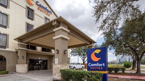 Eingang eines Comfort Suites Hotels mit überdachter Zugangsbereiches, einem Schild und einem Parkplatz.