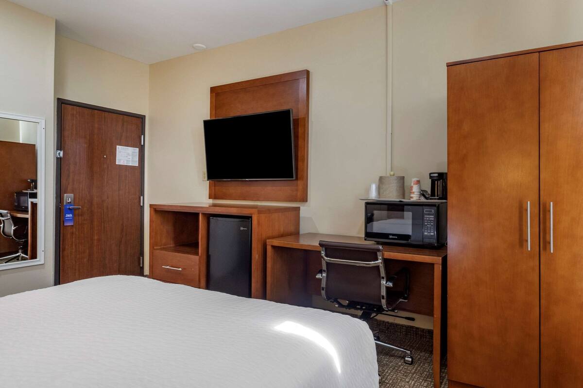 Een hotelkamer met een bed, een bureau met een computer, een televisie, een magnetron en een kledingkast.