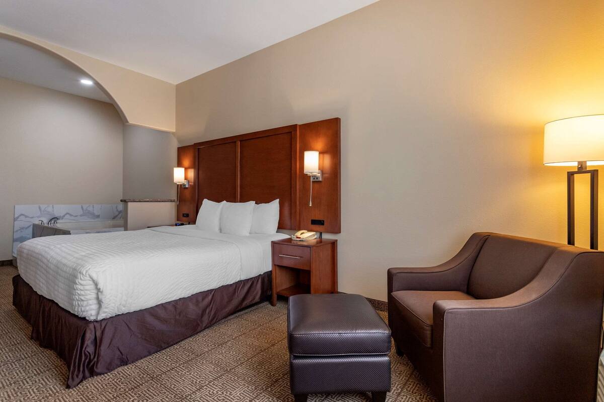 Een hotelkamer met een groot bed, een nachtkastje met een lamp, een stoel en een klein tafeltje.