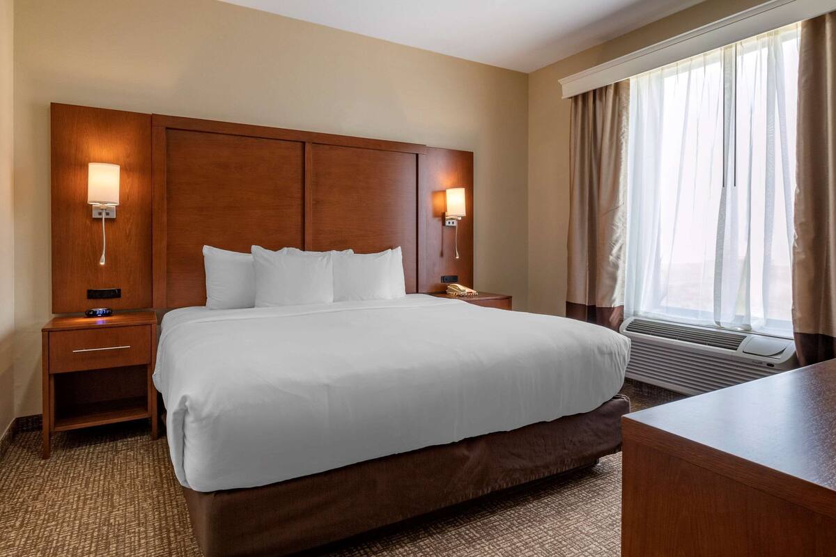 Een hotelkamer met een groot bed, twee nachtkastjes, een bureau en een raam met gordijnen.