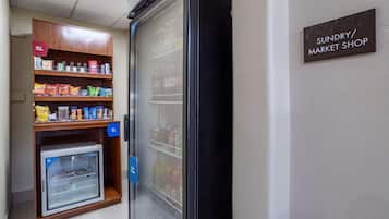 Une petite vitrine réfrigérée contenant des collations et des boissons, un mini-réfrigérateur et une enseigne indiquant un magasin de produits divers.