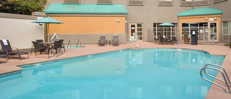 A swimming pool with lounge chairs and umbrellas, surrounded by a building with multiple windows and a door.