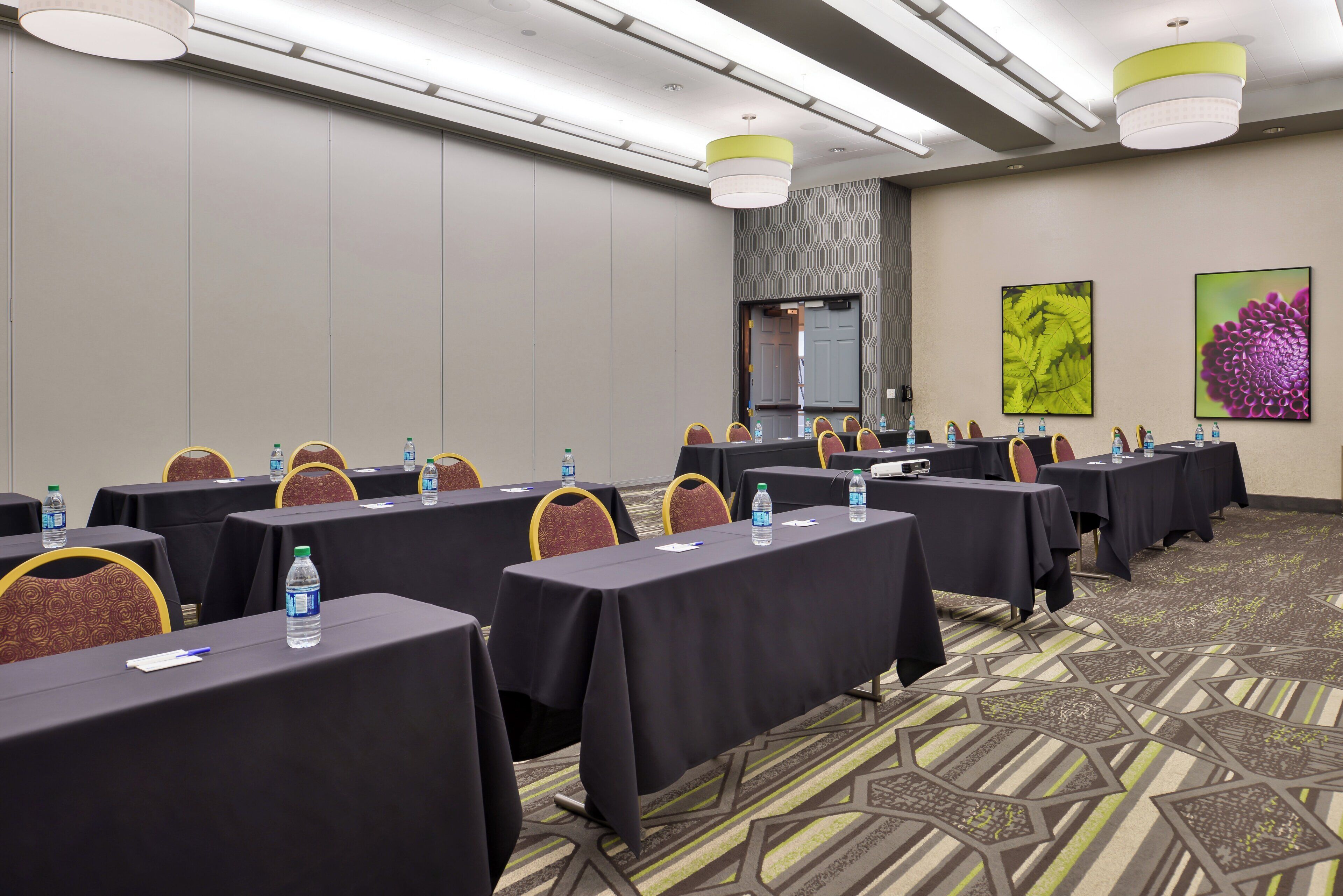 A conference room with multiple tables, chairs, water bottles, and a projector.