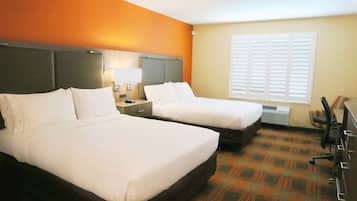 Ein Hotelzimmer mit zwei Betten, einem Nachttisch mit Lampe, einem Fenster mit Jalousien und einer Rezeption.