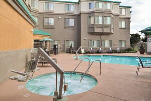 Zona de piscina de un hotel con jacuzzi, sillas de descanso y un edificio con múltiples ventanas y balcones al fondo.