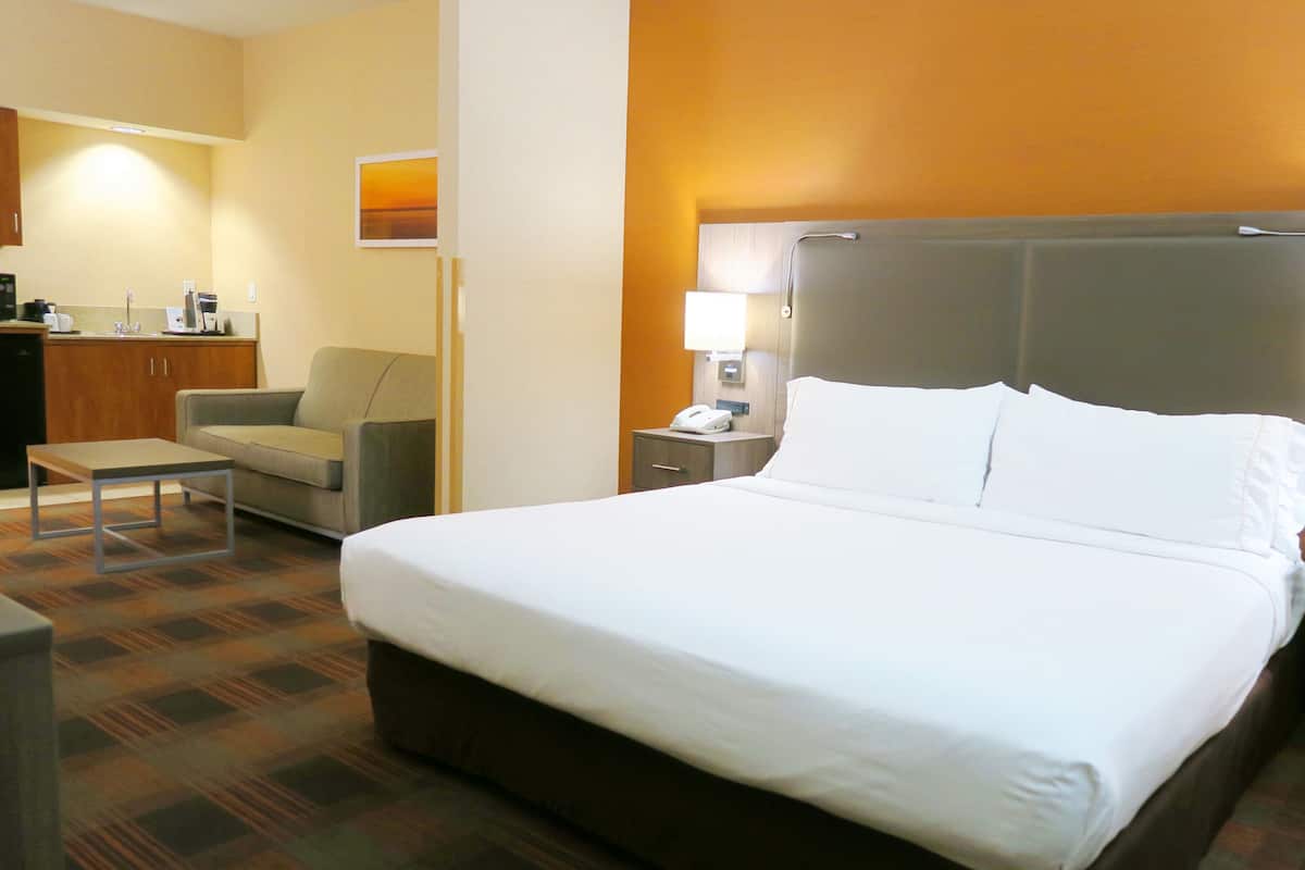 Une chambre d’hôtel avec un grand lit, un bureau, une chaise et une petite kitchenette.