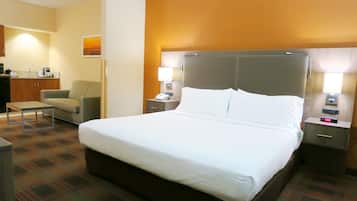 A hotel room with a large bed, a desk, a chair, and a small kitchenette.