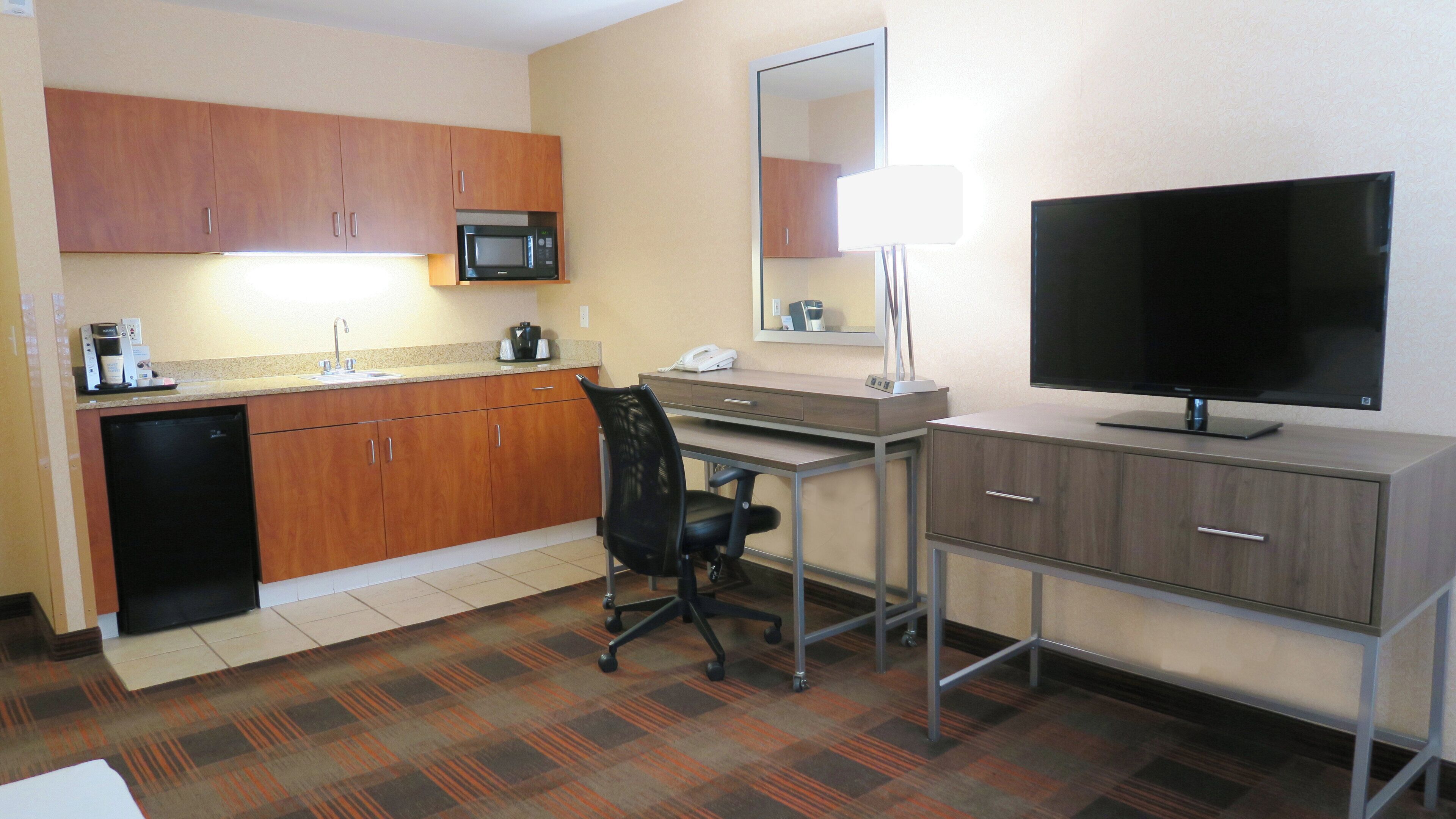 A hotel room with a kitchenette, a desk with a chair, a television, and a large mirror.