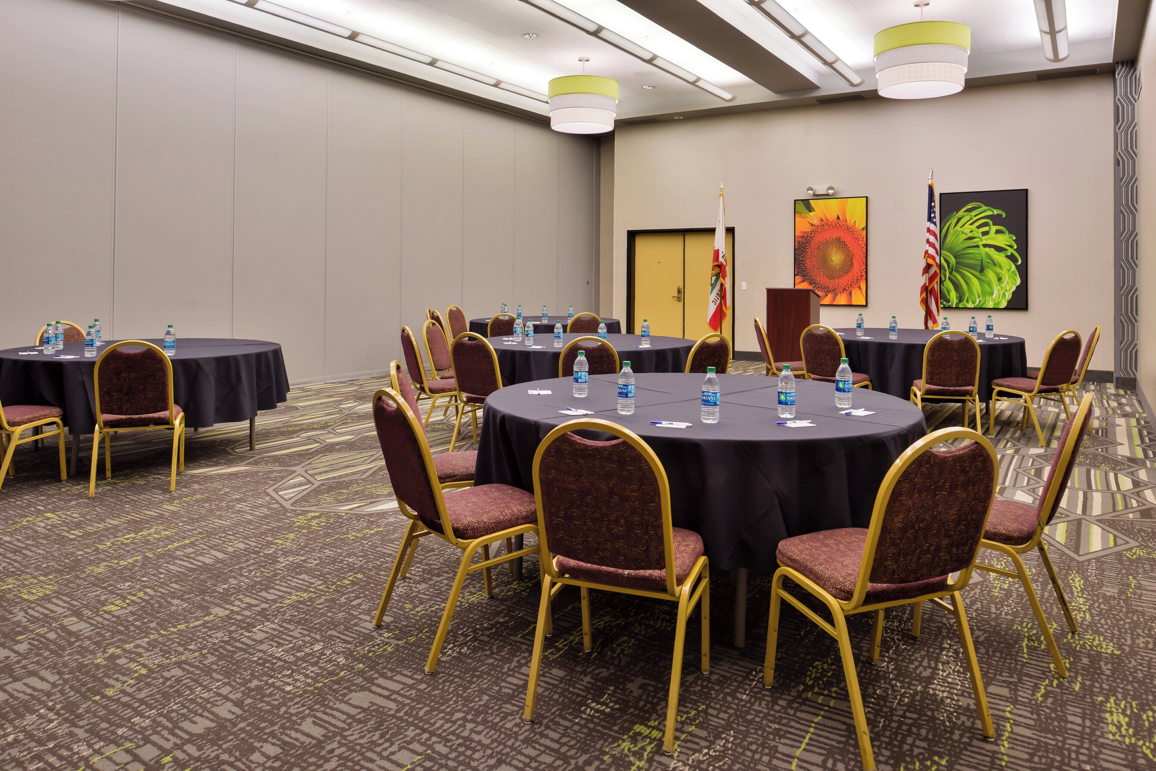 Un salón de conferencias con mesas redondas, sillas, botellas de agua y banderas.