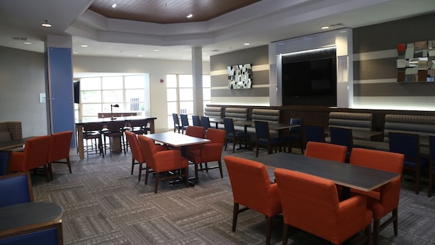 A modern dining area with multiple tables and chairs, a large flat-screen TV, and a patterned carpet. - Holiday Inn Express & Suites Elk Grove Central - Hwy 99 by IHG (Elk Grove)