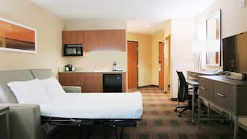 Habitación de hotel con cama, escritorio, silla, microondas, cafetera y televisor.