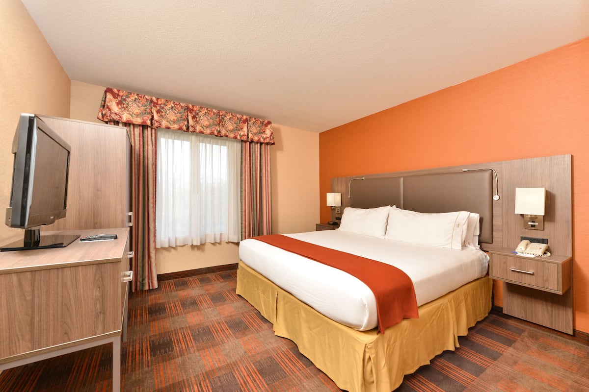 Une chambre d’hôtel comprenant un lit, un bureau avec une télévision, une table de chevet avec un téléphone et une fenêtre avec des rideaux.