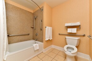 A bathroom with a bathtub, toilet, and grab bars.