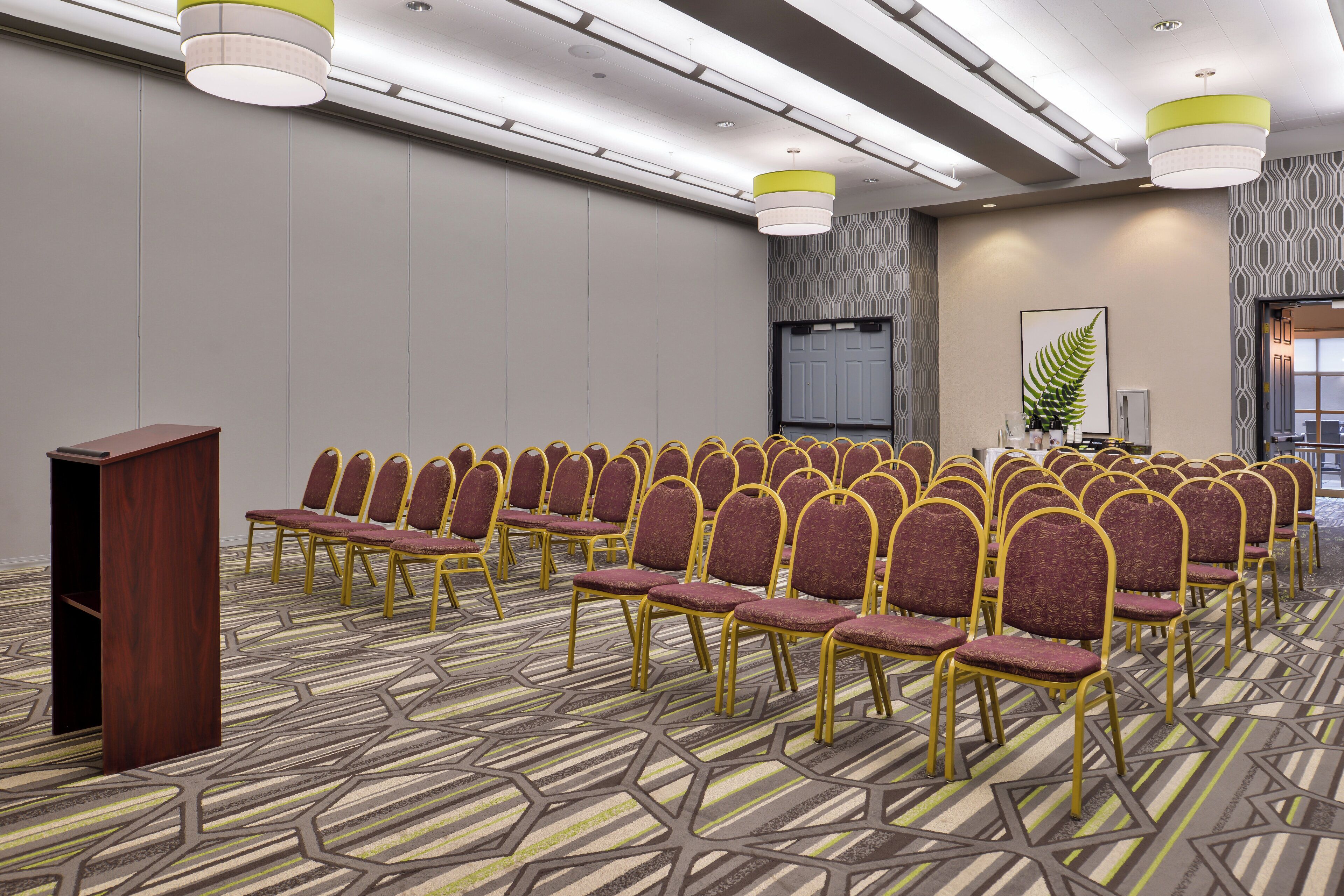 Un salón de conferencias con filas de sillas, un atril y una alfombra estampada.