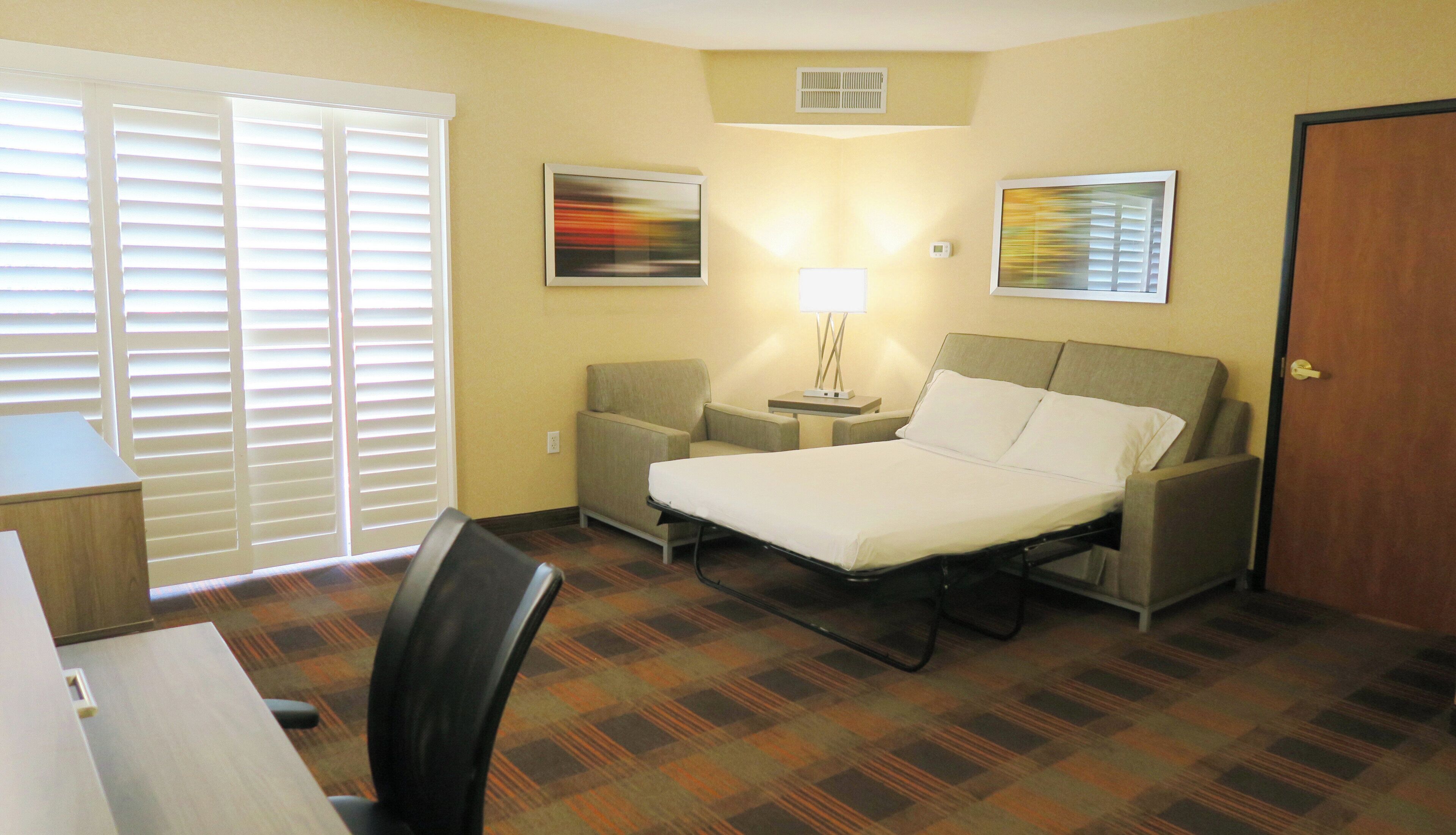 Habitación de hotel con cama, escritorio, silla, lámpara y dos cuadros en la pared.