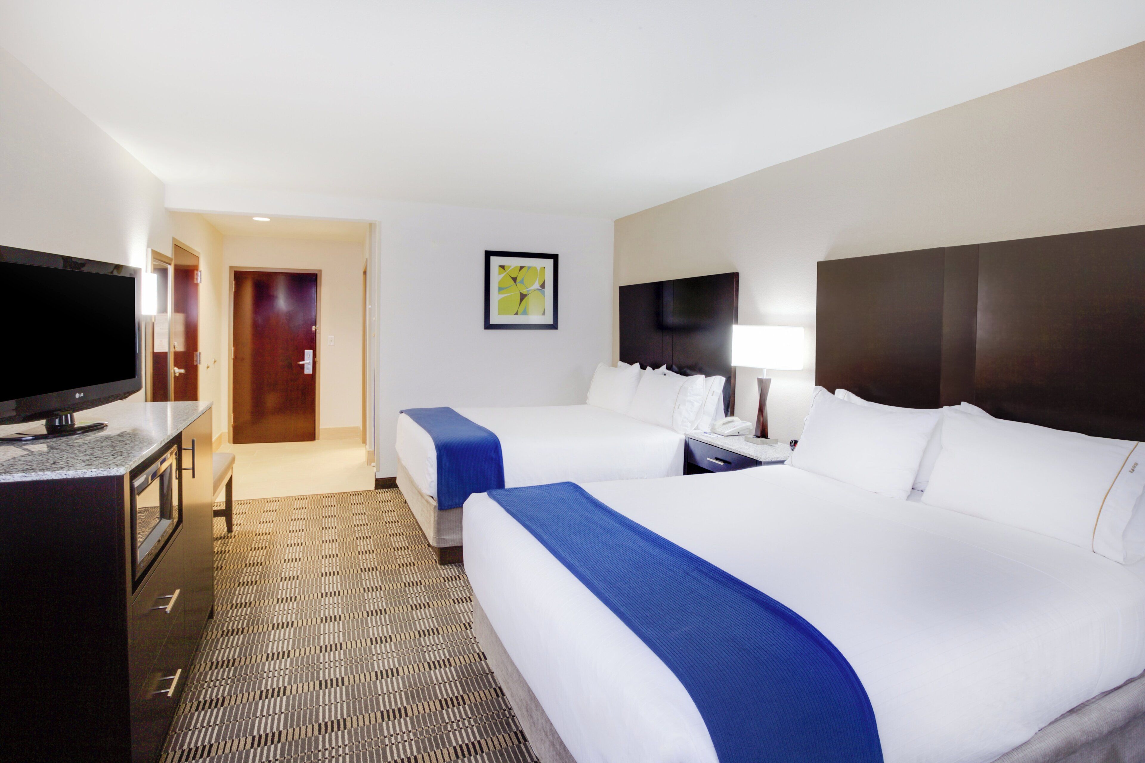 A hotel room with two beds, a television, a desk, and a framed picture on the wall.