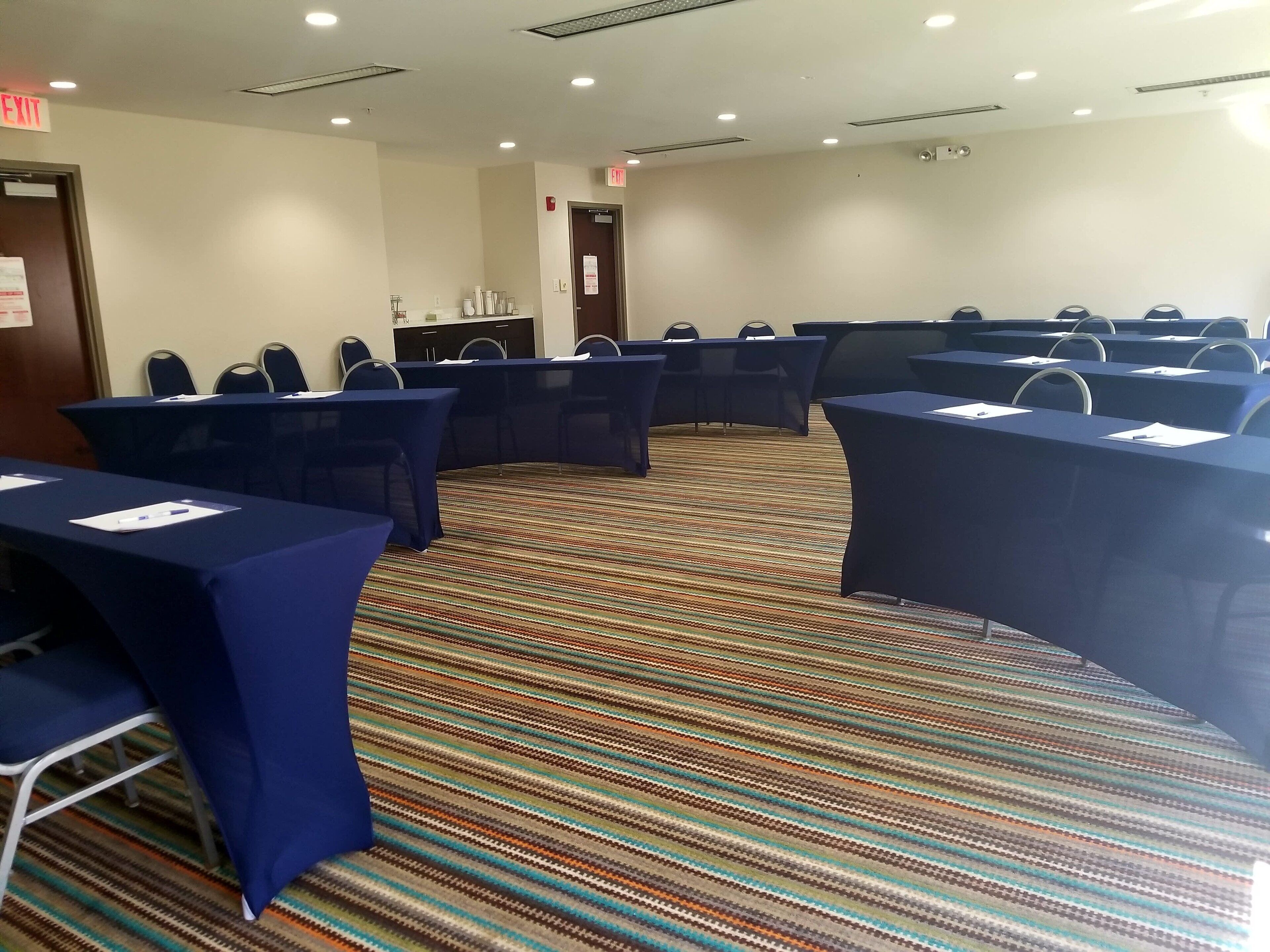 A conference room with multiple tables and chairs, carpeted floor, and ceiling lights.