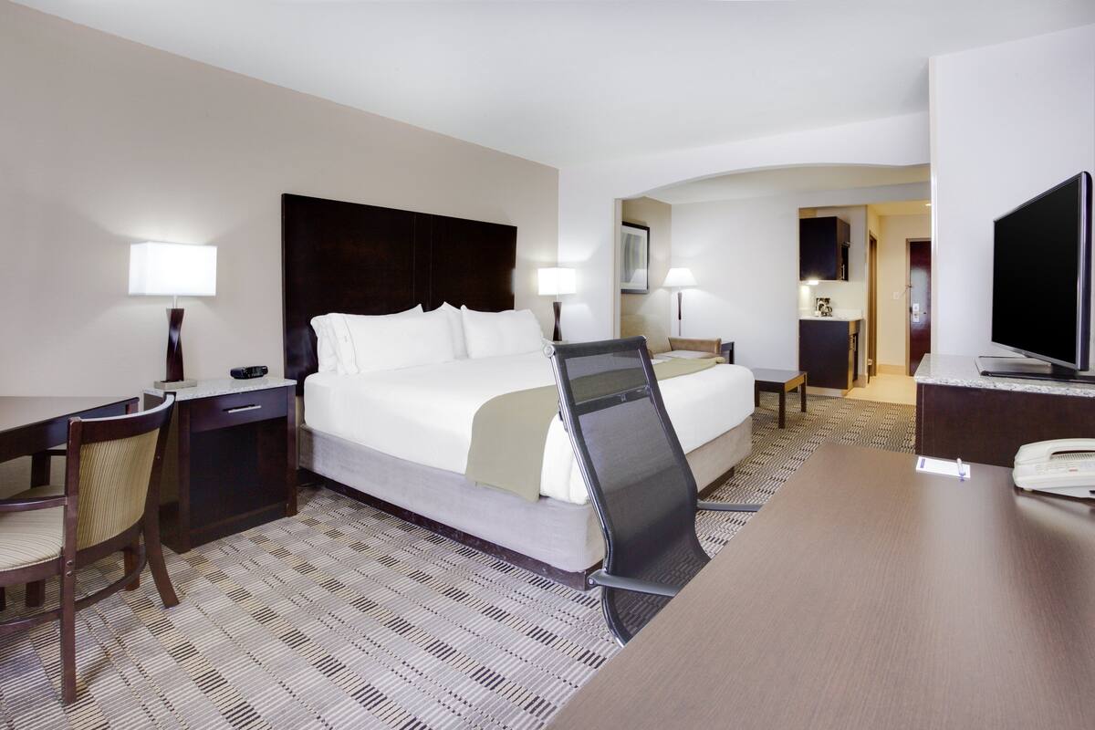 A hotel room with a bed, desk, chair, and a television.
