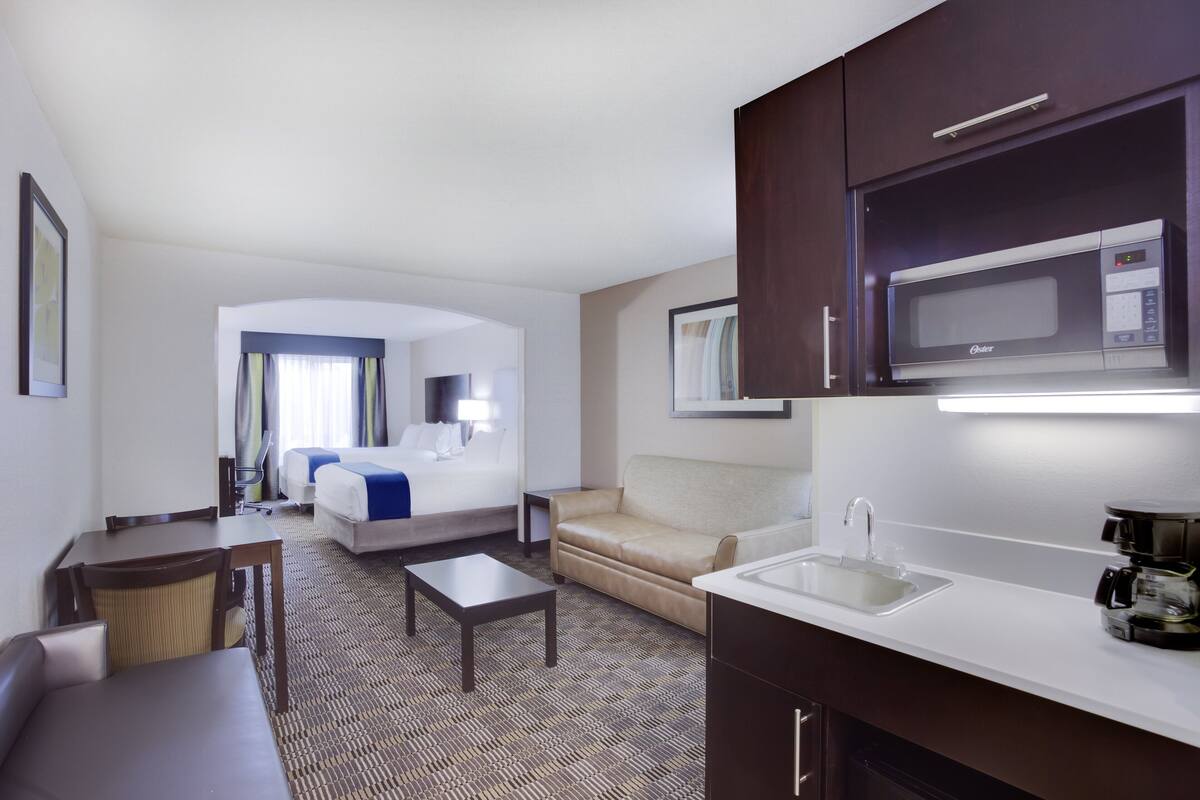 A hotel room with a bed, a sofa, a small table, a kitchenette with a microwave, and a sink.