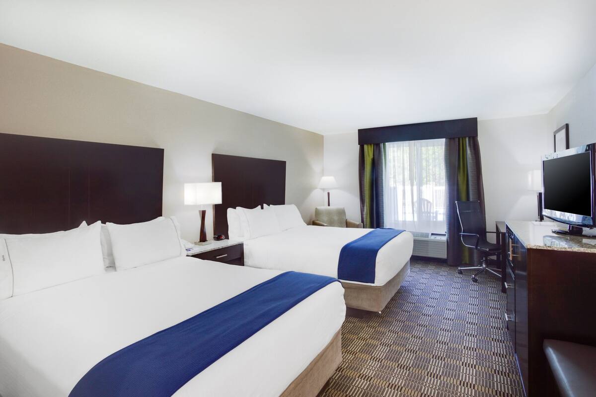A hotel room with two beds, a desk, a chair, a television, and a window with curtains.
