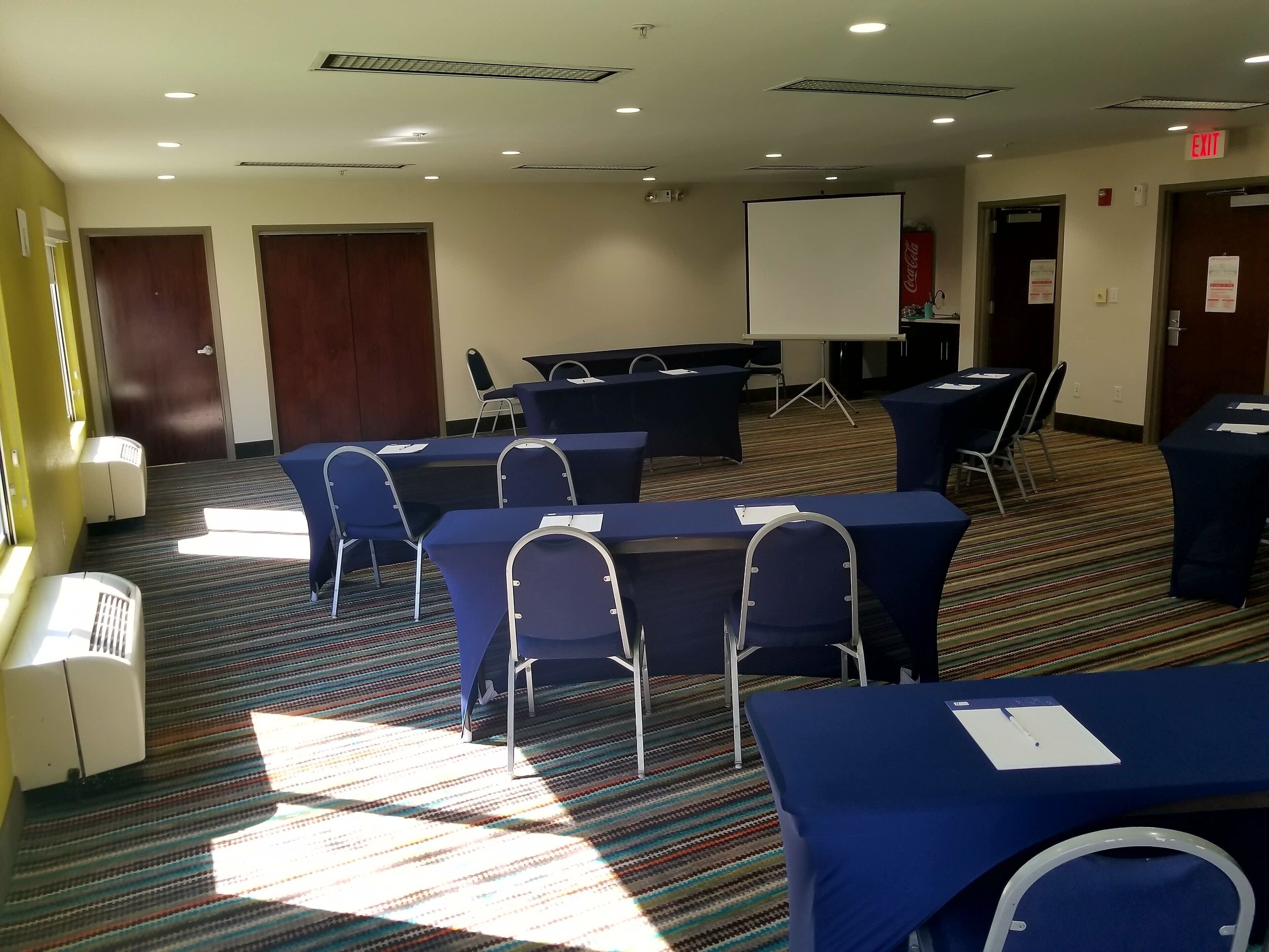 Un salón de conferencias con mesas, sillas, una pizarra y un letrero de salida.