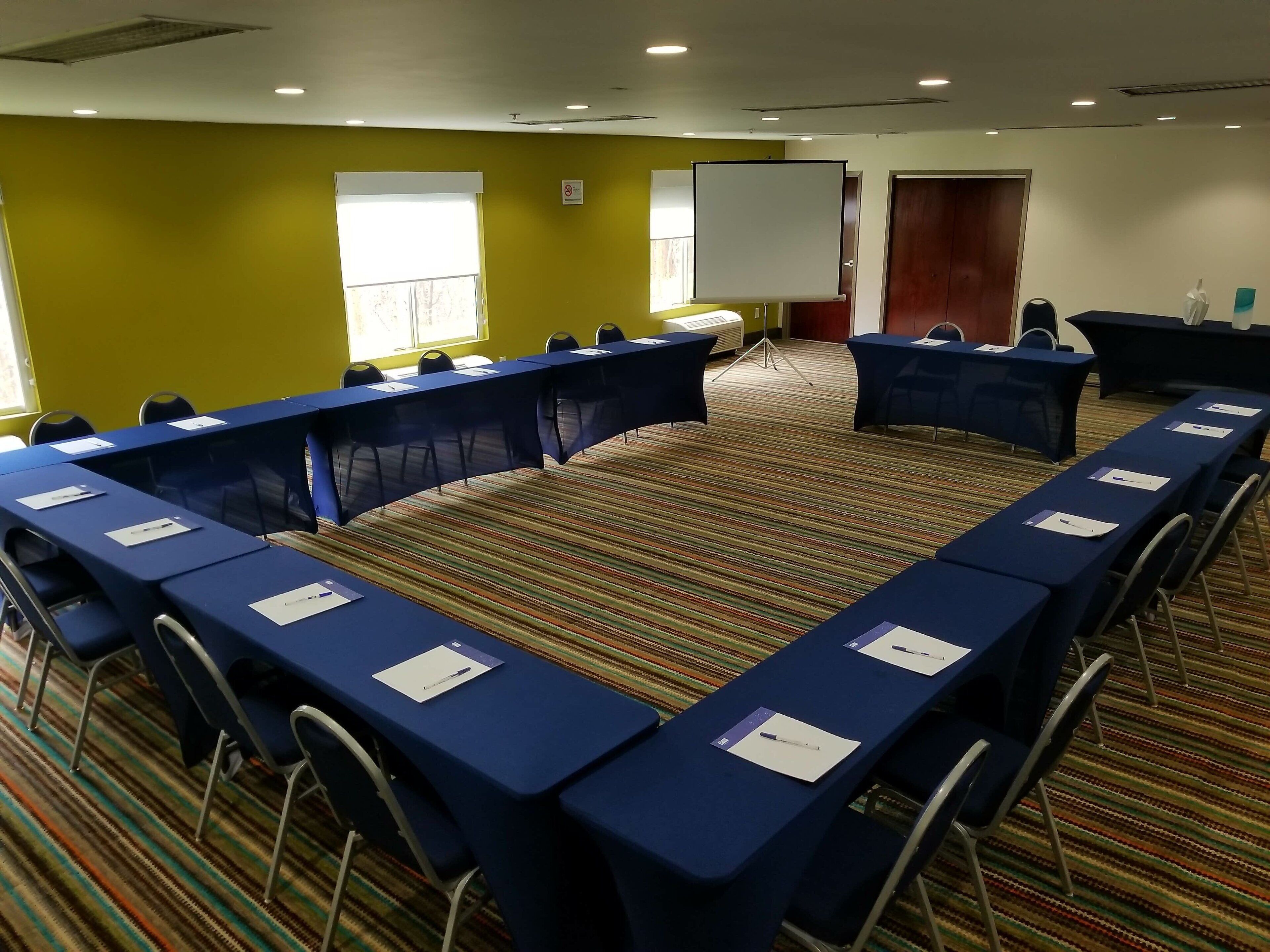 Uma sala de conferência com uma mesa comprida, cadeiras e uma tela de projetor.