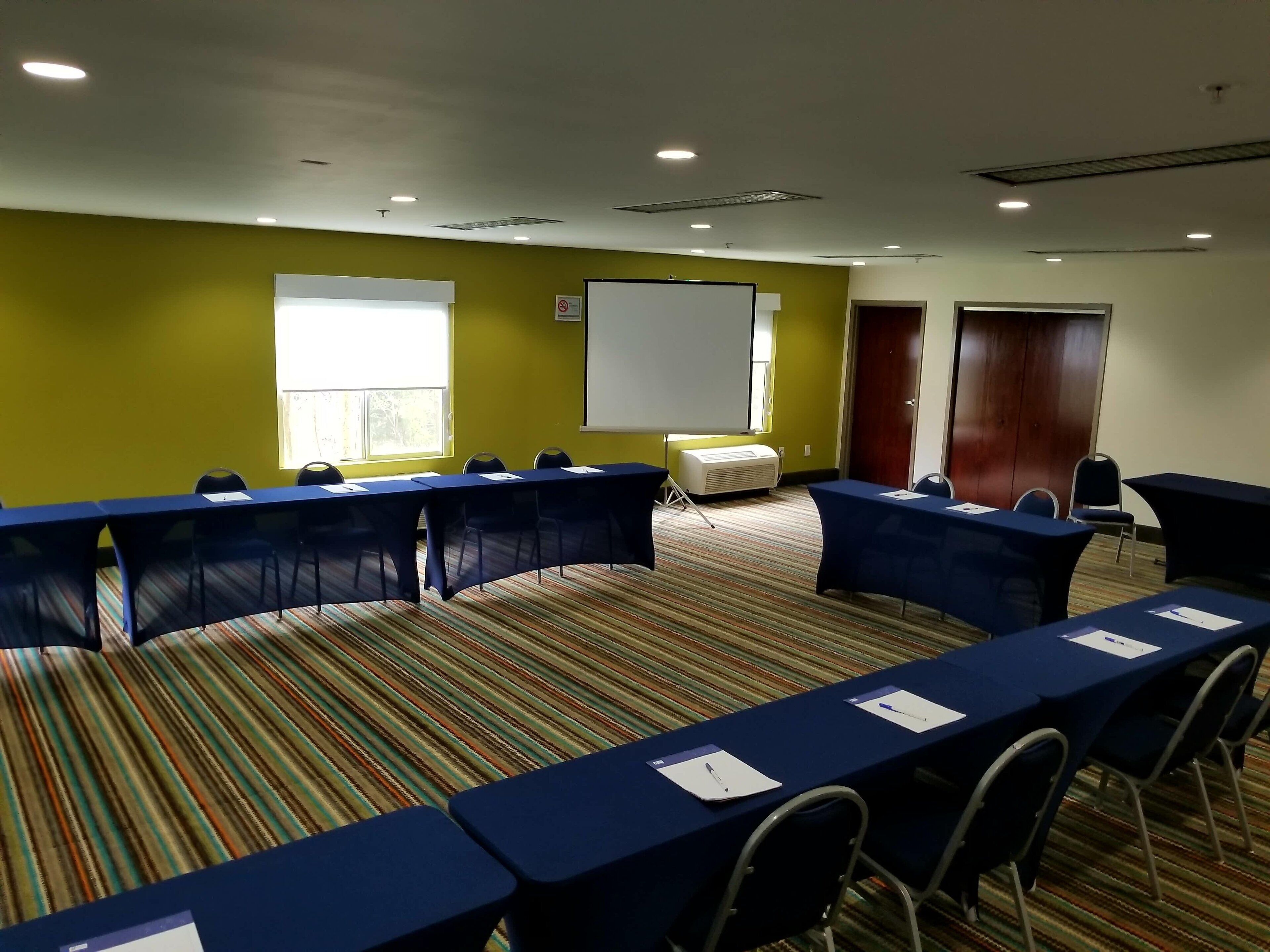 A conference room with a long table, chairs, a projector screen, and a whiteboard.