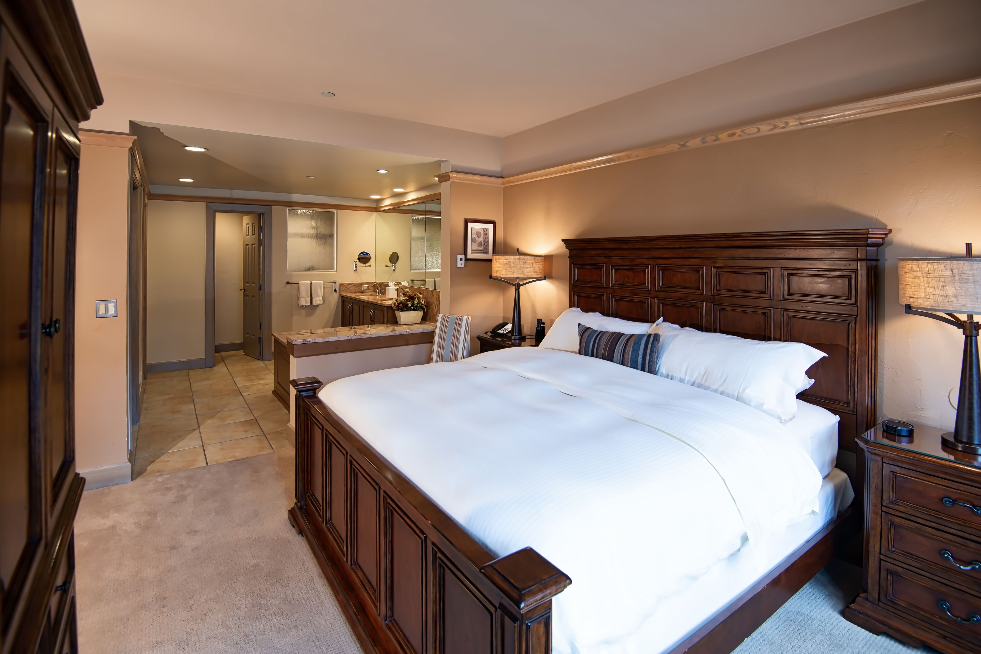 A spacious bedroom with a large bed, wooden headboard, and a nightstand with a lamp.
