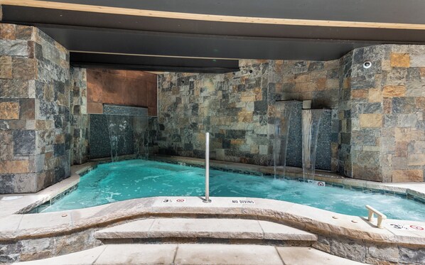Un jacuzzi con un muro de piedra como fondo y una piscina.