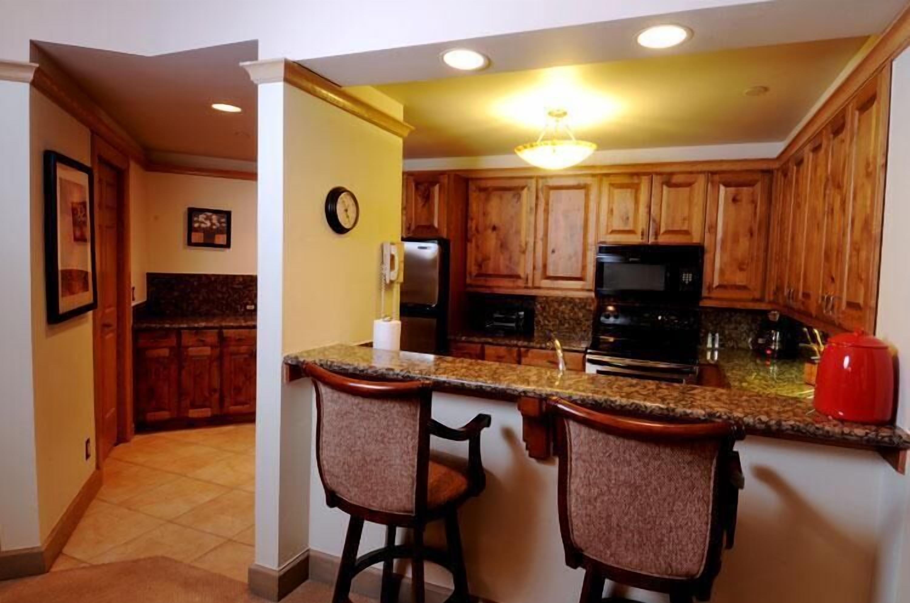 Una cocina con gabinetes de madera, encimera de granito y dos taburetes de bar.