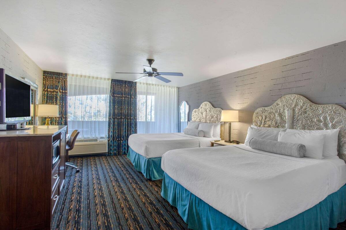 A hotel room with two beds, a desk with a TV, a ceiling fan, and a window with curtains.