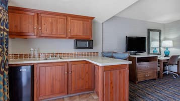 A compact kitchen with wooden cabinets, a microwave, a sink, and a small refrigerator.