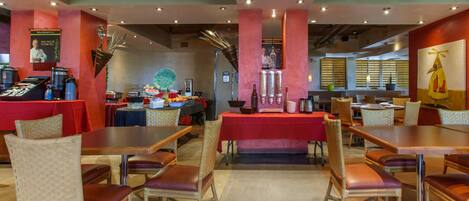 A restaurant with multiple tables and chairs, a buffet area, and a counter with food items.