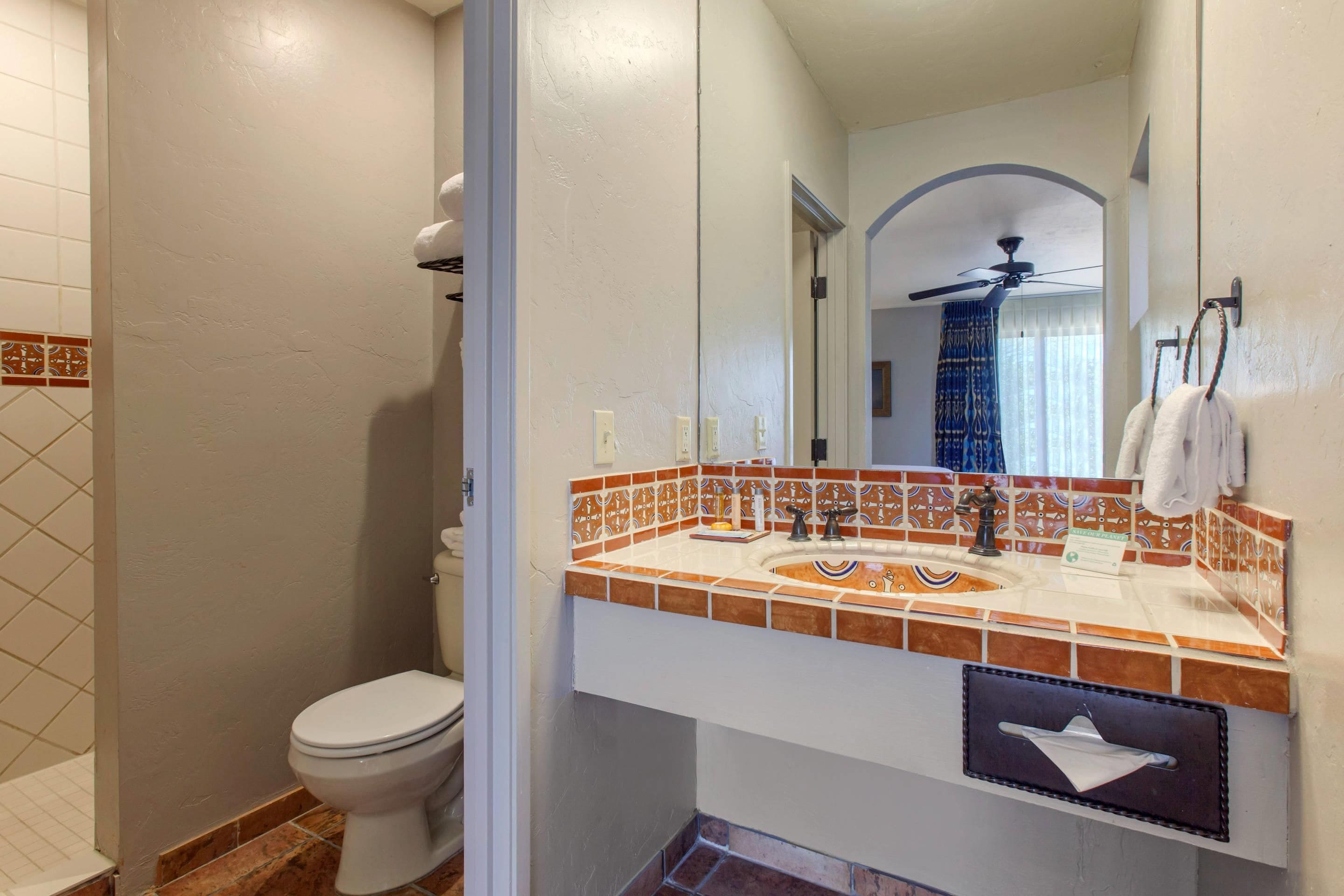 A bathroom with a toilet, a sink with a mirror, and a shower area.