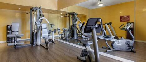 A gym with various exercise equipment, a mirror wall, and wooden flooring.