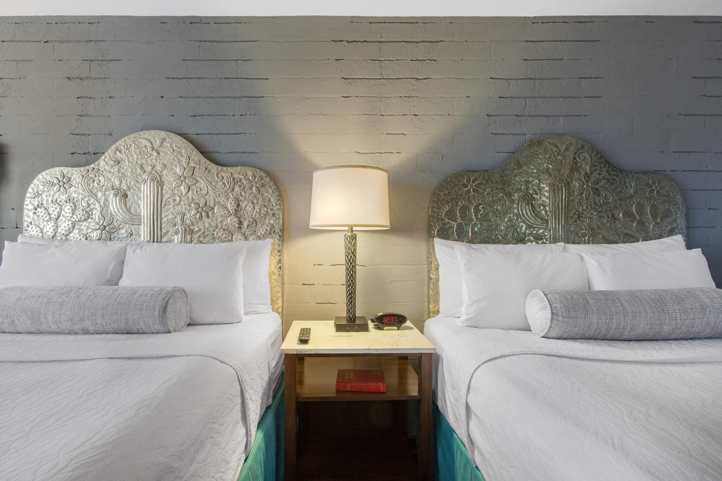 A hotel room with two beds, a nightstand with a lamp, and a clock.