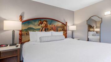 A hotel room with a large bed, two bedside lamps, a nightstand, a digital clock, a mirror, and a wall-mounted painting.