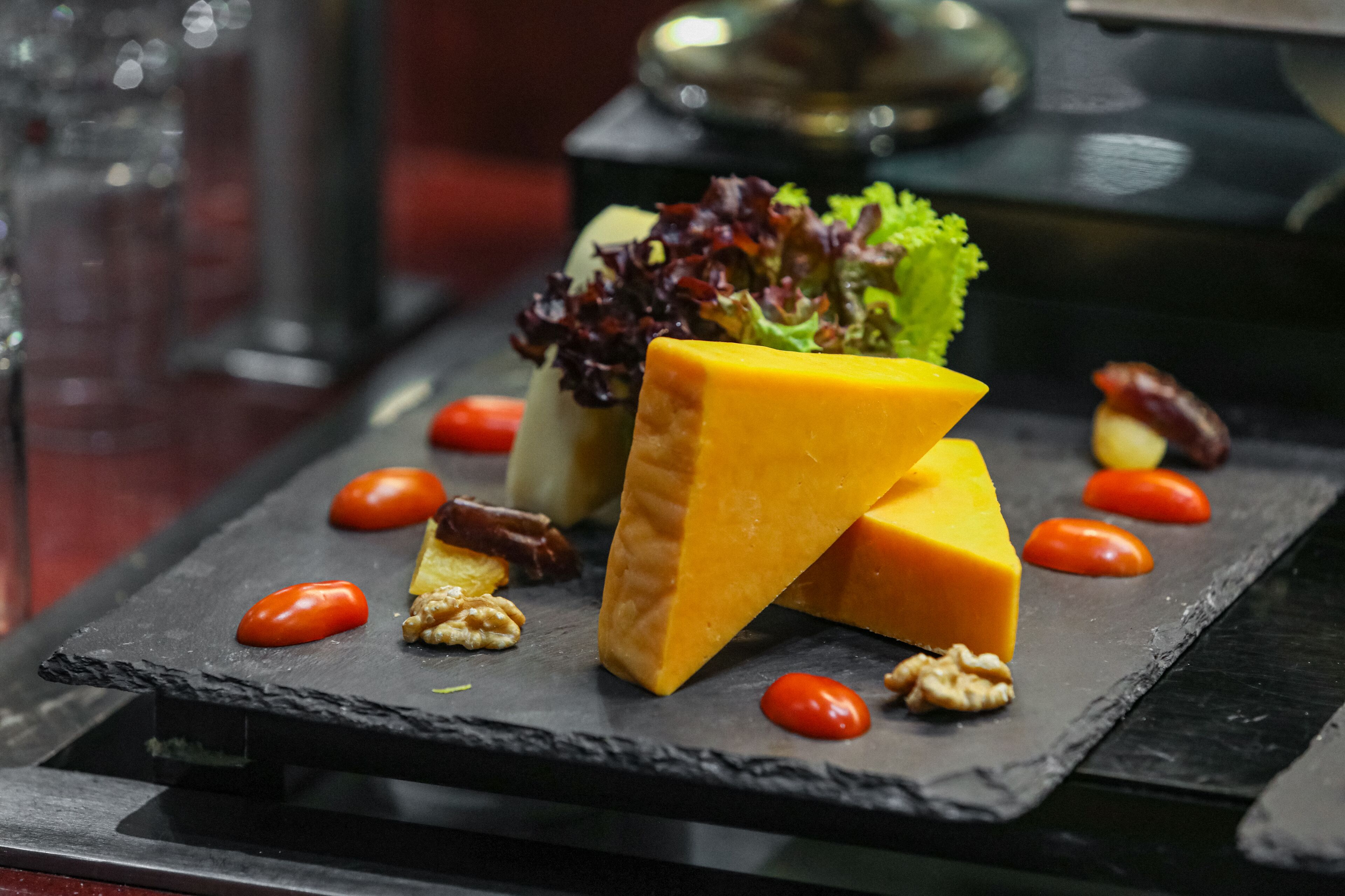 A black slate serving board with a wedge of cheese, cherry tomatoes, walnuts, and a leafy salad.
