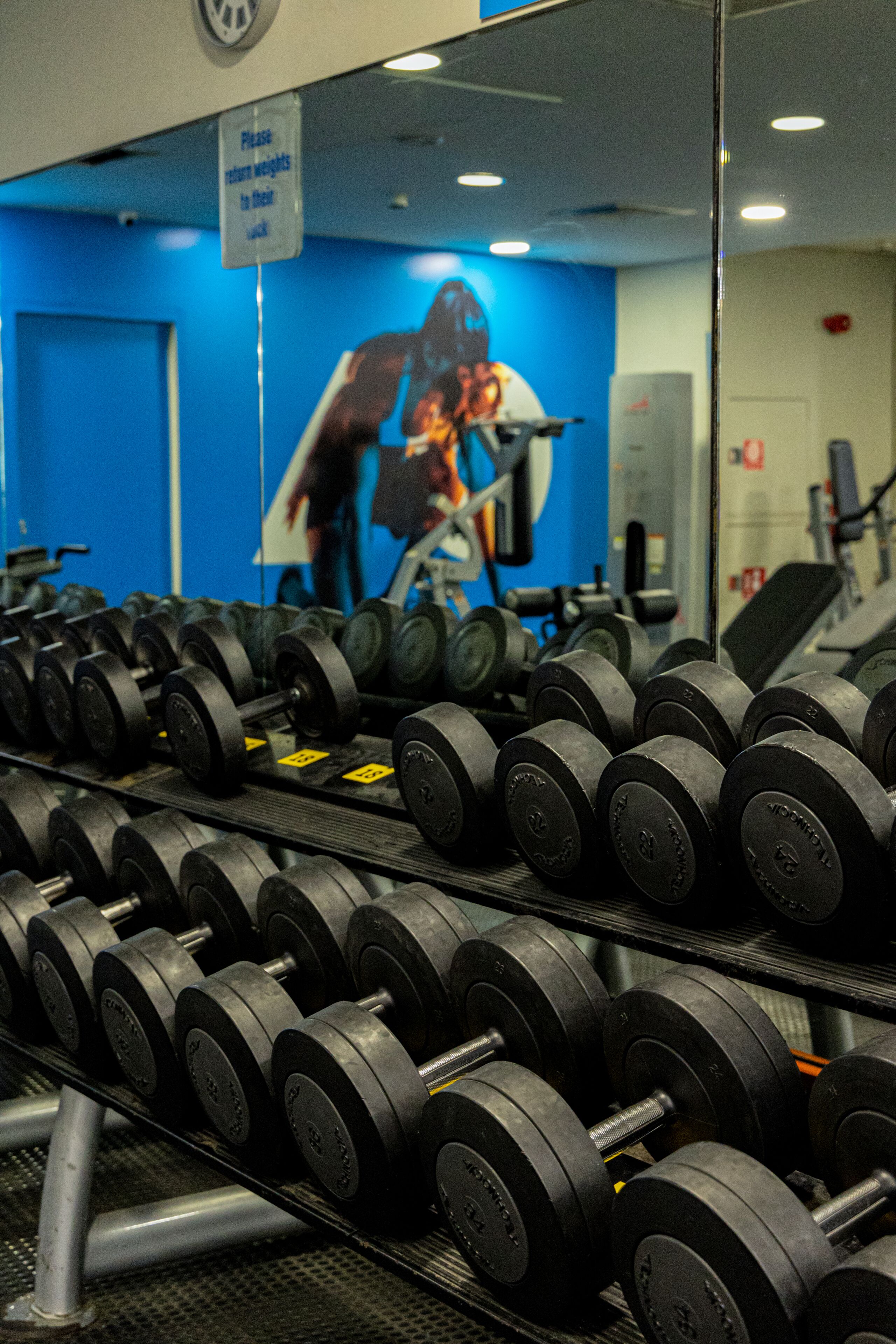 A gym with rows of dumbbells and a sign instructing to return weights to their rack.