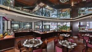A restaurant with multiple dining tables set for guests, a buffet area with various food items, and a view of the city through large windows. - Crowne Plaza Hotel Beirut by IHG (Beirut)