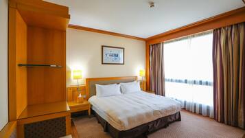 A hotel room with a large bed, wooden headboard, two bedside tables with lamps, a framed picture on the wall, and a window with curtains.