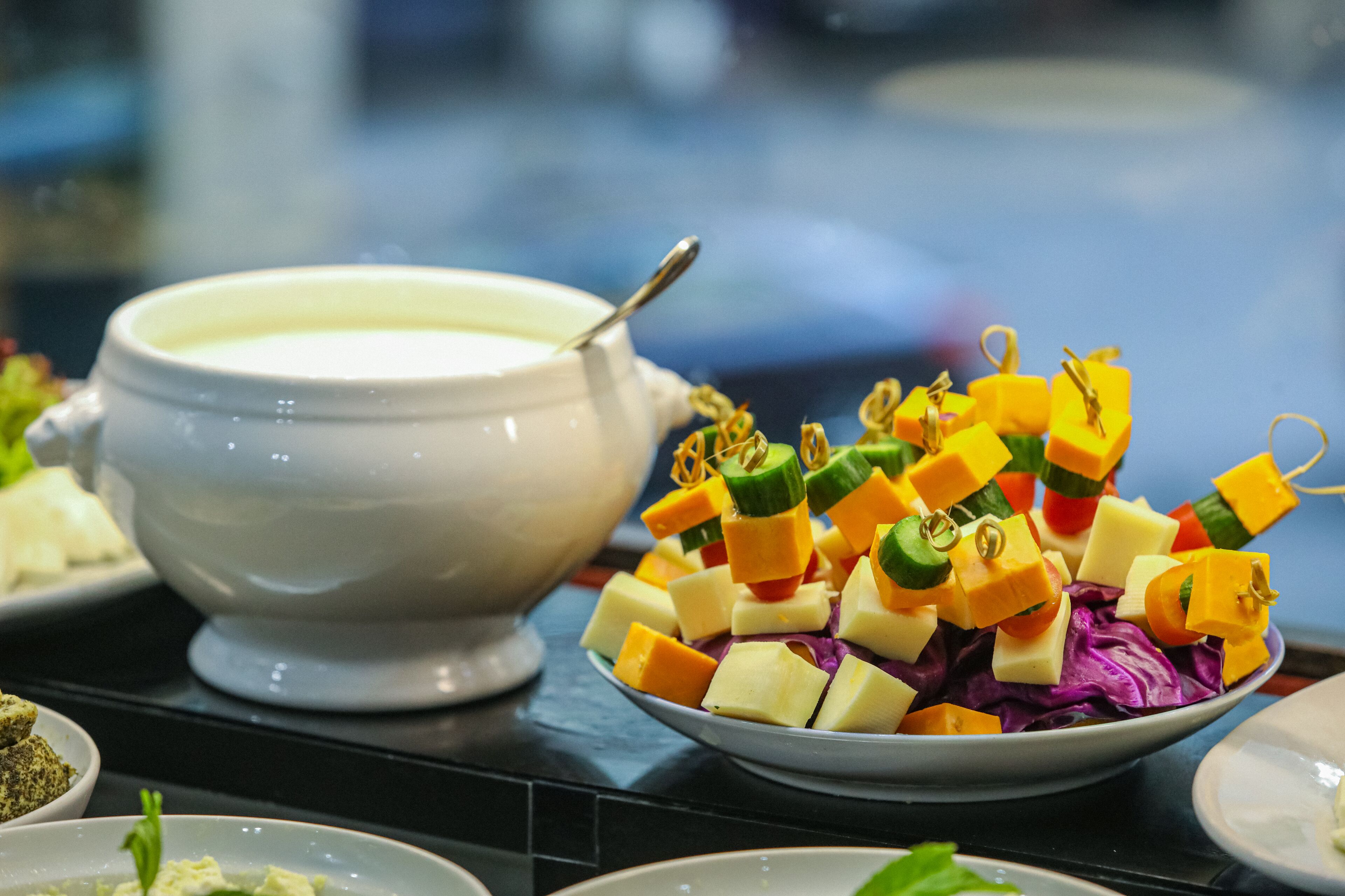 Une table de buffet proposant une variété de plats, notamment un bol de soupe et une assiette de cubes de fromage de différentes couleurs.