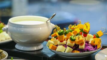 Une table de buffet proposant une variété de plats, notamment un bol de soupe et une assiette de cubes de fromage de différentes couleurs.