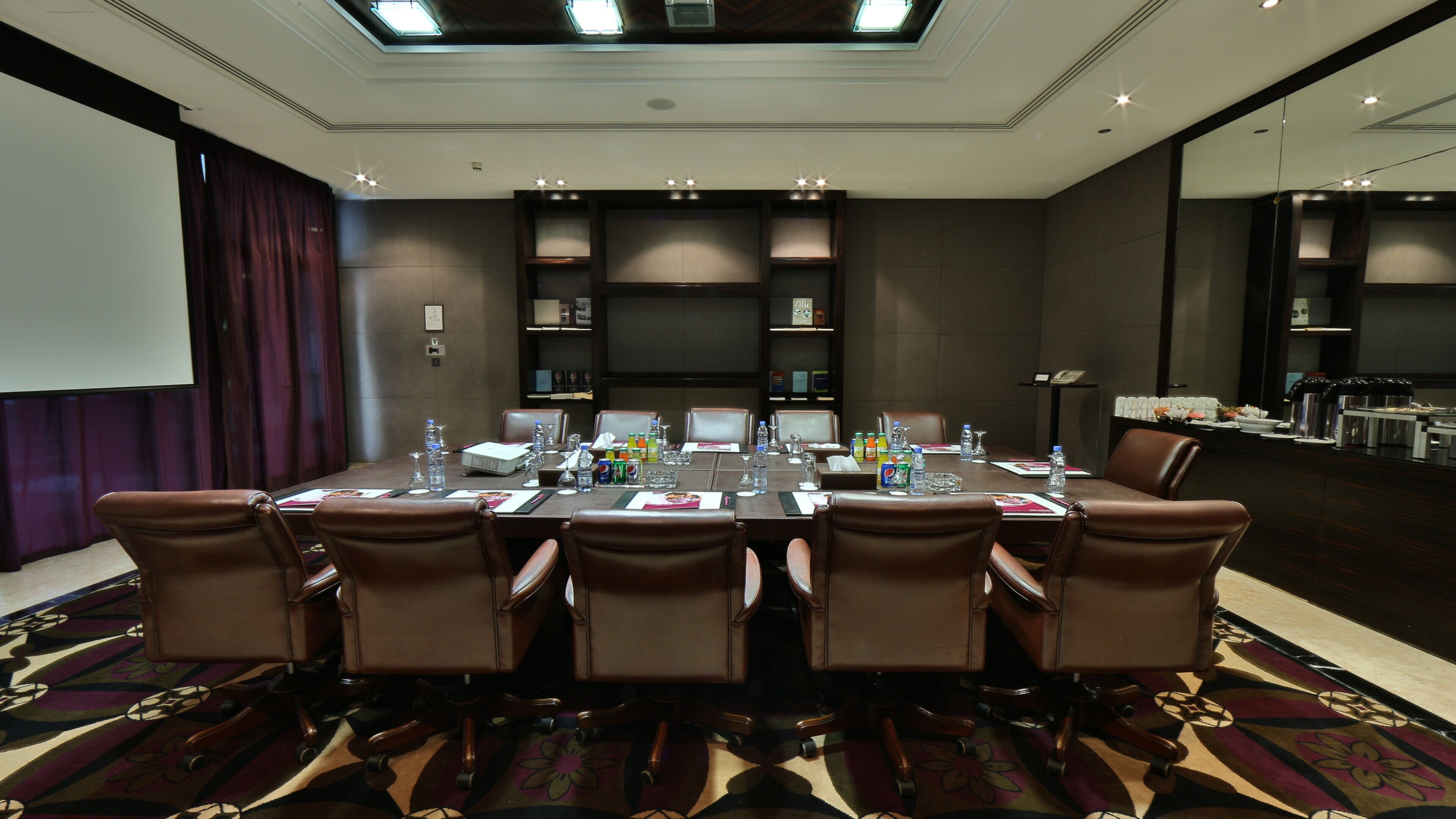 A conference room with a long table, chairs, and a projector screen.