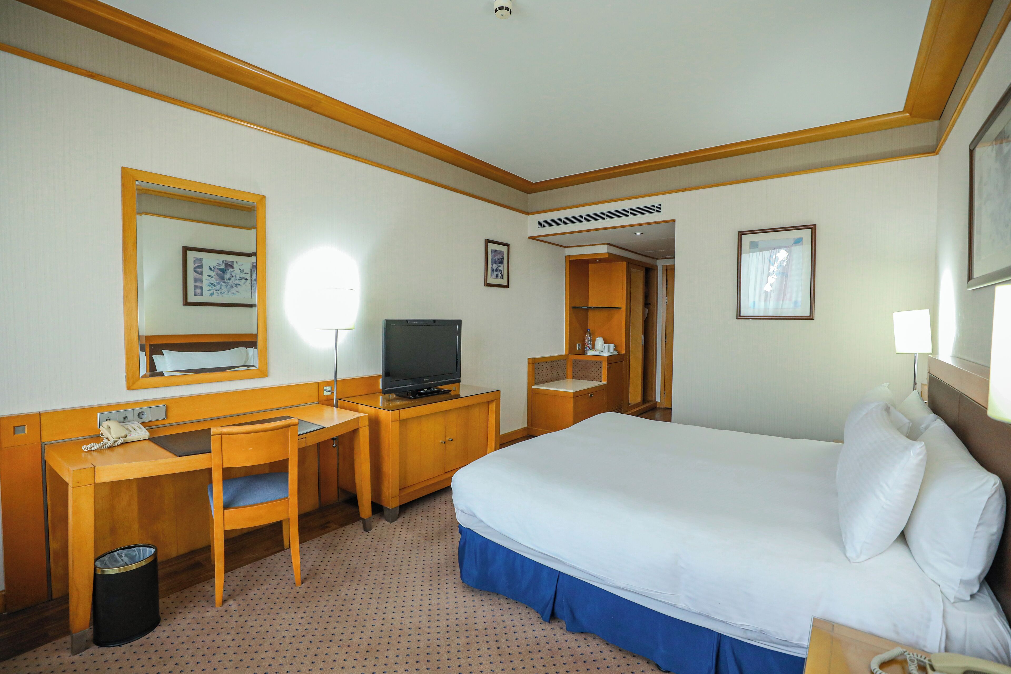 A hotel room with a bed, desk, chair, television, and a trash bin.