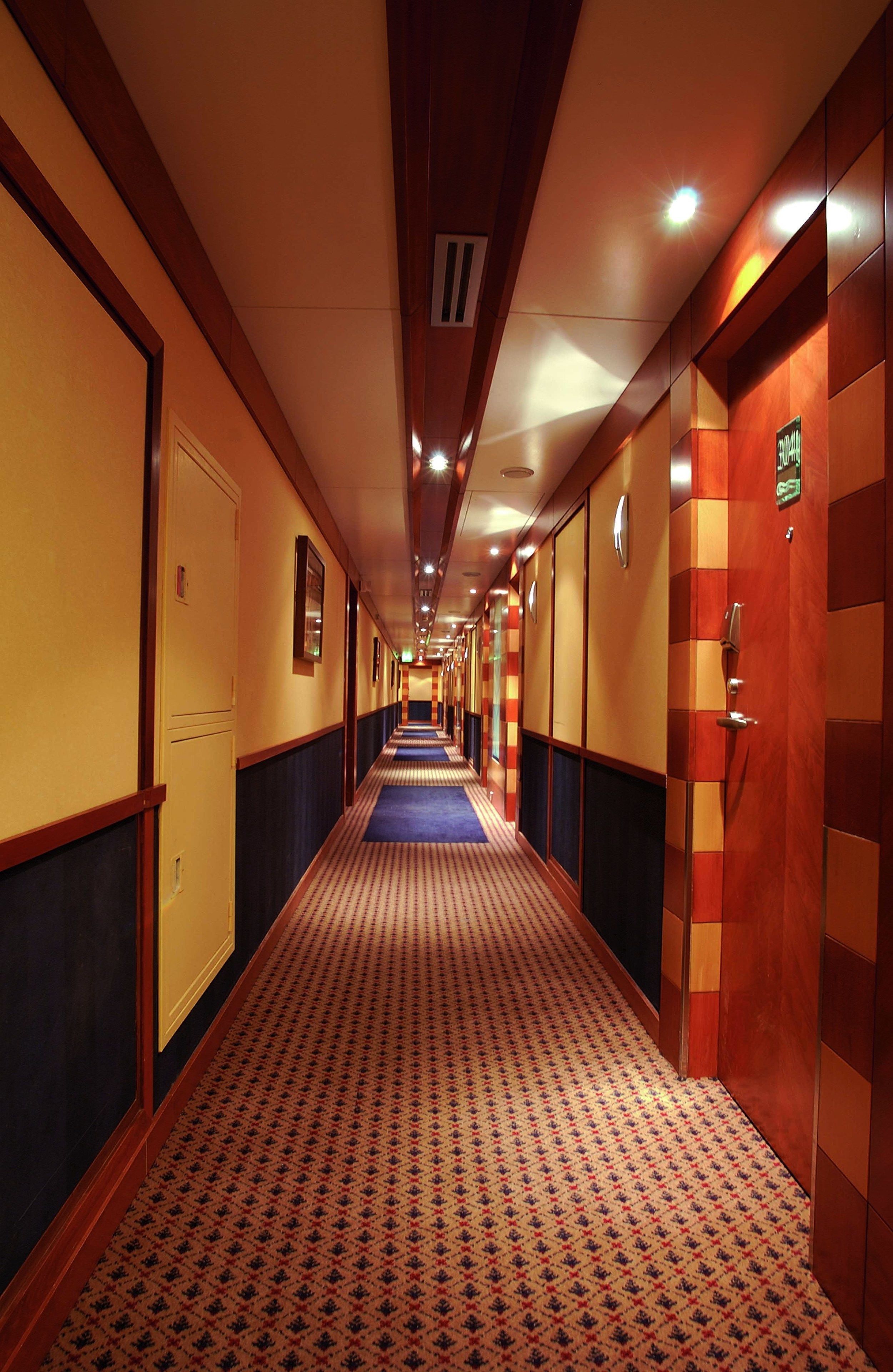 A hotel corridor with a patterned carpet, wooden paneling, and doors on both sides.