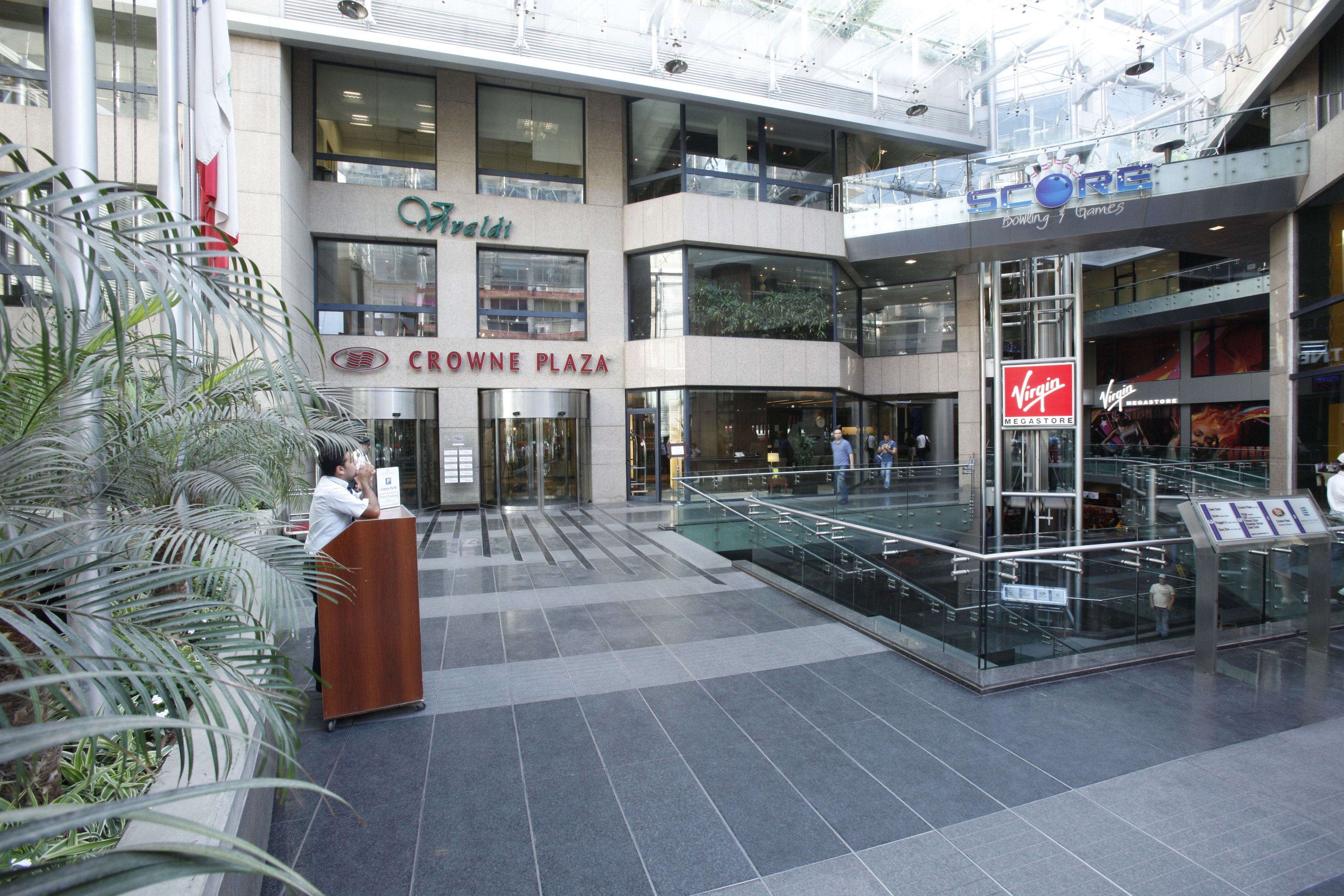 Un centro comercial de varios niveles con un atrio de cristal, que incluye tiendas como Crocne Plaza y Score.