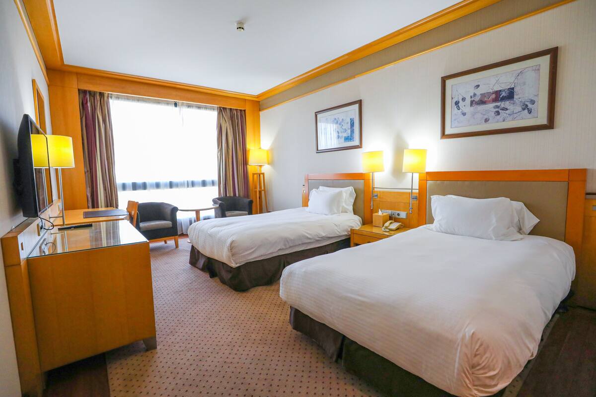 Quarto de hotel com duas camas, uma escrivaninha, uma cadeira e uma televisão.