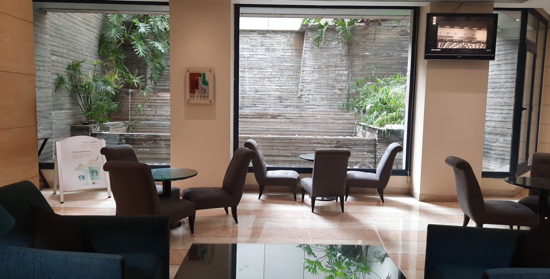 A modern indoor seating area with multiple chairs and tables, a coffee station, and a view of a brick wall and greenery outside.